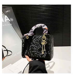 Détail d'un sac à main noir à texture d'écailles avec foulard en soie et breloque dorée