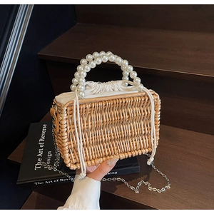 Detail of woven straw handbag featuring large pearl handle and metal chain strap
