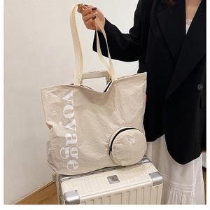 Détail d'un grand sac cabas beige en toile lavée avec texte voyage sur une valise
