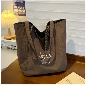 Close-up of brown oversized tote bag featuring leopard print straps and merci typography
