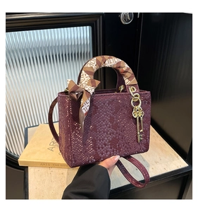 Détail du sac à main bordeaux à motif peau de serpent avec foulard en soie et breloque dorée