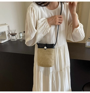 Detail of hand-woven straw crossbody phone bag with black leather flap and pearl button
