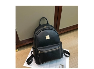 Detail of black leather backpack with white stitching and square gold logo plaque