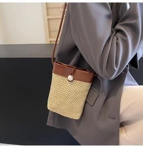 Detail of straw woven crossbody bag with brown leather flap and pearl closure on model