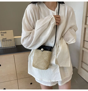 Detail of mini straw crossbody bag with white pearl accent and black leather trim