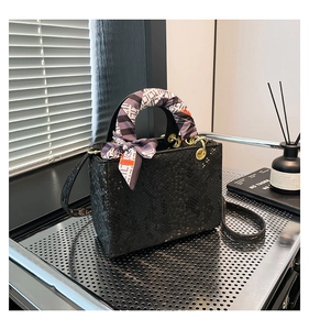 Détail du sac à main noir motif écailles avec ferrures dorées et poignée en soie