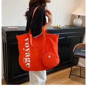Détail d'un sac cabas en nylon orange vif avec imprimé voyage et petit porte-monnaie