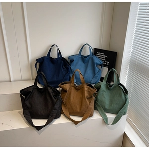 Minimalist canvas tote bags shown in five colors on a white display stand with wide straps
