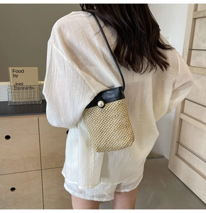 Woven straw crossbody bag with pearl buckle and leather strap on a model's back