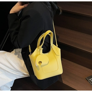 Detail view of yellow lychee grain leather bucket bag with elephant charm on wooden stairs