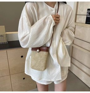 Close-up of woven straw crossbody bag with brown leather flap and pearl buckle detail