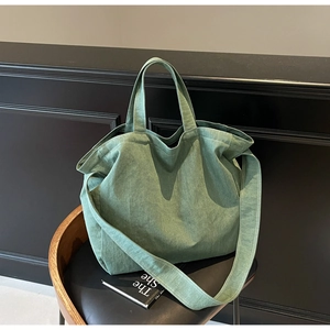 Detail of grey-green canvas tote bag with wide shoulder strap on a black chair