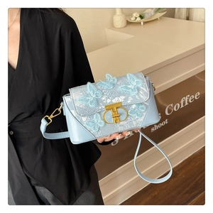 Close-up of light blue small square bag featuring 3D butterfly lace appliques and gold T-lock