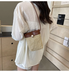 Detail of woven straw crossbody bag with pearl button closure and brown leather strap