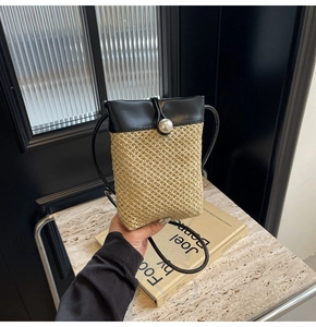 Detail of straw woven crossbody phone bag with black leather flap and pearl clasp