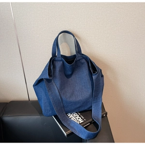 Close-up of a large navy blue denim tote bag on a black sofa with double strap design