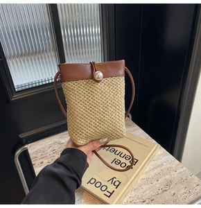 Detail of hand-woven straw crossbody bag with brown leather trim and a white pearl buckle