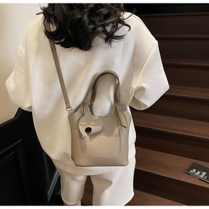 Detail view of taupe lychee leather tote bag with elephant charm on wooden steps
