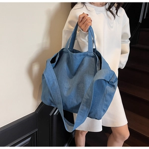 Lifestyle shot of an oversized blue denim tote bag worn as a shoulder bag on a model