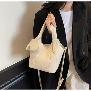 Close-up of beige lychee grain leather bucket bag with cute elephant charm and handles