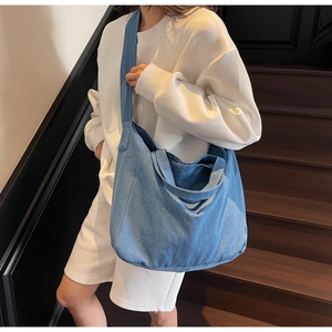 Detail of blue denim tote bag worn by a model in a cozy indoor setting on wooden stairs