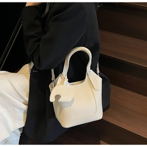 Close-up of cream leather bucket bag with bird charm on dark stairs with a model