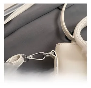 Detail view of the silver metal hook and polished leather strap on the cream bucket bag