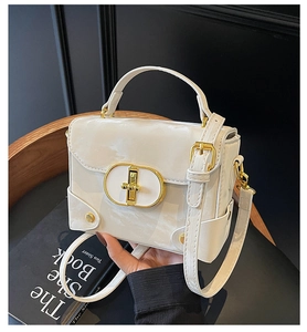 Detailed view of cream patent leather bag featuring a gold oval twist lock and handle