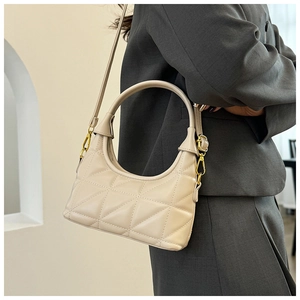 Detail of cream quilted handbag with geometric patterns and shiny gold metal hardware