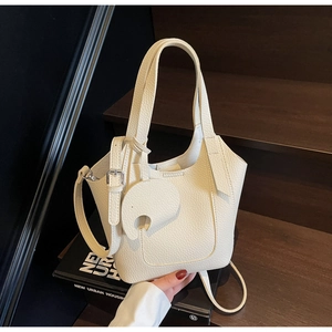 Detail of off-white lychee grain leather bucket bag with creative elephant charm on stairs