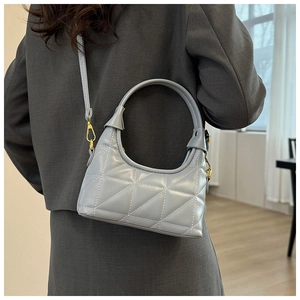 Detail view of a quilted light grey Hobo bag with gold hardware worn by a model
