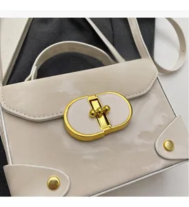 Detailed macro of a cream leather handbag with a golden oval rotating lock and metal ball top