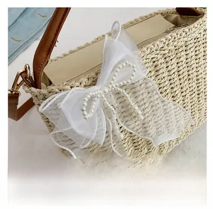 Close-up of woven straw bag featuring white lace bow, pearls, and brown leather handles
