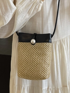 Crossbody woven straw phone bag with contrast leather trim and pearl closure on white dress
