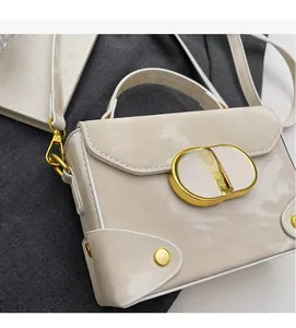 Detail view of cream-white leather box bag with gold oval buckle and fine shoulder strap