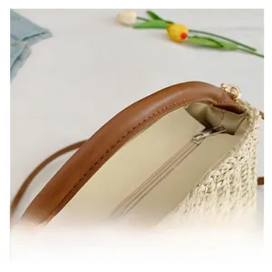 Detail of beige woven straw bag with brown faux leather handles and silver zipper closure