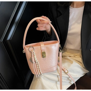 Détail du sac seau rose avec fermoir doré et breloque tissée porté par le mannequin