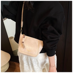 Detail shot of beige shoulder bag featuring golden logo and stylish leather tassel