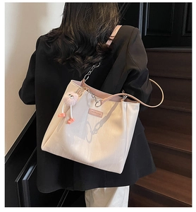 Close-up of beige tote bag featuring pink lining, metal chain, and cute plush charm detail