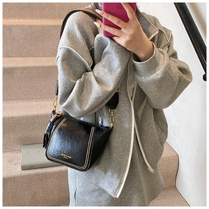 Close-up of black glossy crossbody bag with double gold stud hardware and wide strap