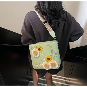Close-up of intricate 3D floral embroidery featuring sunflowers on a green bucket bag