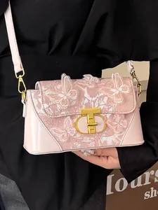 Pink crossbody bag with 3D butterfly embroidery and gold metal clasp worn by a model