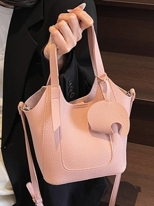 Pink lychee grain leather bucket bag with elephant charm held by model in black suit