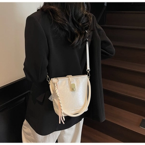 Détail du sac seau blanc cassé avec fermoir rotatif doré et pompon décoratif tressé