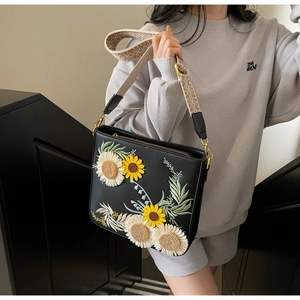 Detailed view of sunflower embroidery on a black bucket bag with a woven strap