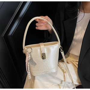 Sac seau beige moderne avec boucle en métal et pendentif décoratif porté par mannequin