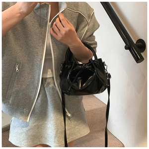 Polished oil wax leather bucket bag with bow detail held by model in casual wear
