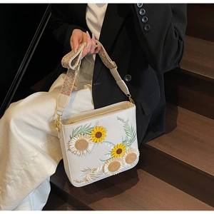 Macro shot of a white bucket bag with sunflower 3D embroidery and ethnic woven strap