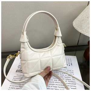 Detail of off-white quilted shoulder bag with gold hardware and curved handle