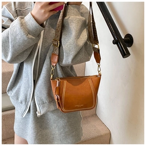 Detail view of brown PU leather crossbody bag with gold rivets and woven shoulder strap